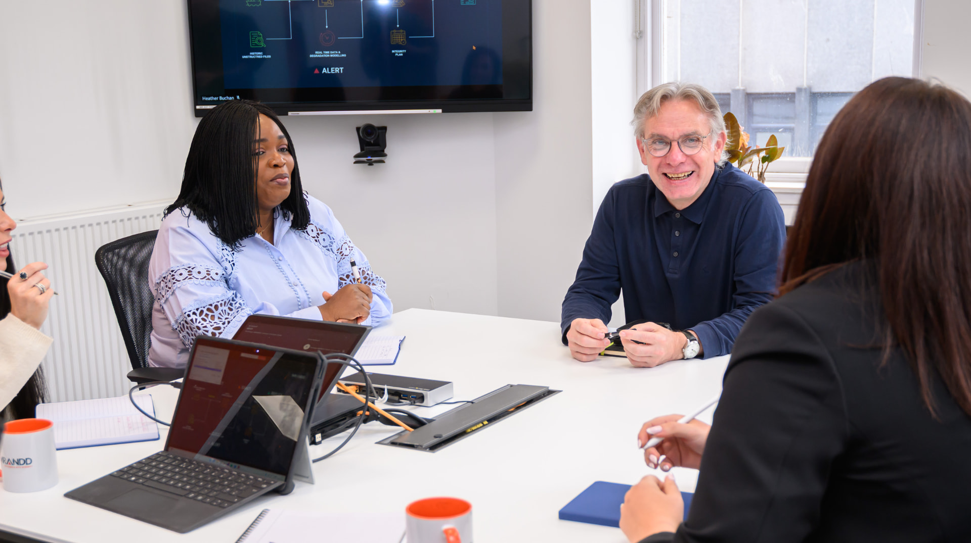 Imrandd colleagues in discussion around a meeting room table, with a data workflow diagram on the screen behind them